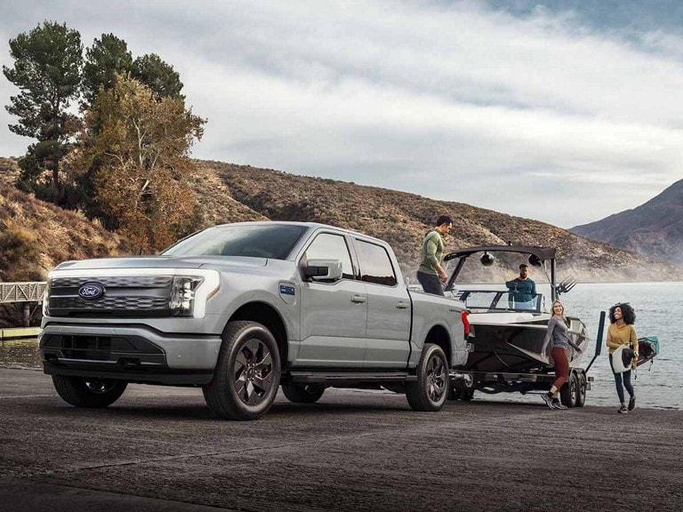 A light blue 2025 Ford F-150 Lightning® pickup truck towing a boat out of a mountain lake