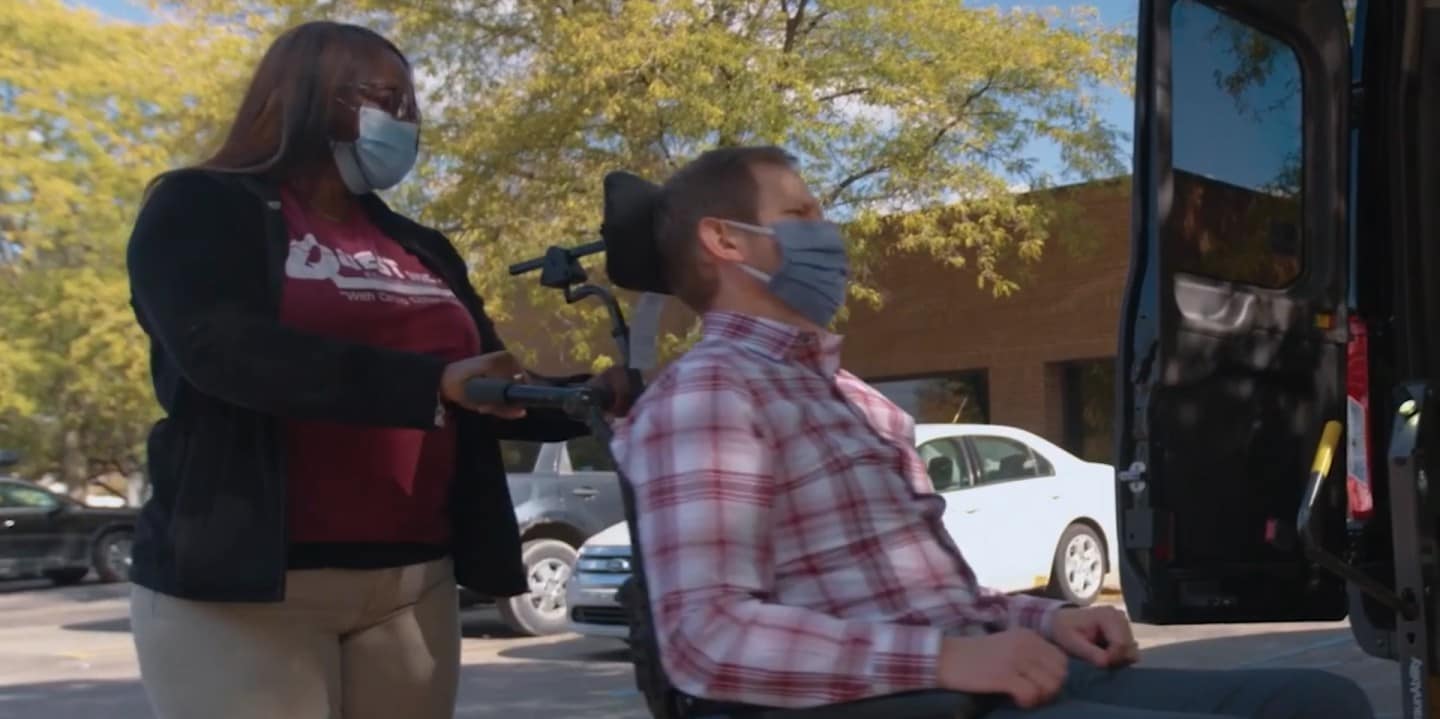 A woman is pushing a wheelchair with a man sitting on it towards an ambulance.