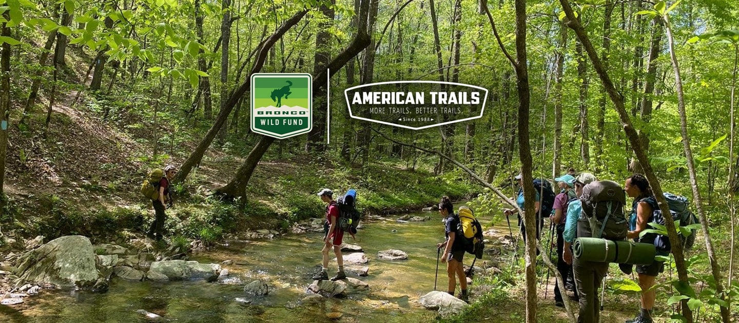 Group of campers crossing a creek by stepping on rocks and boulders