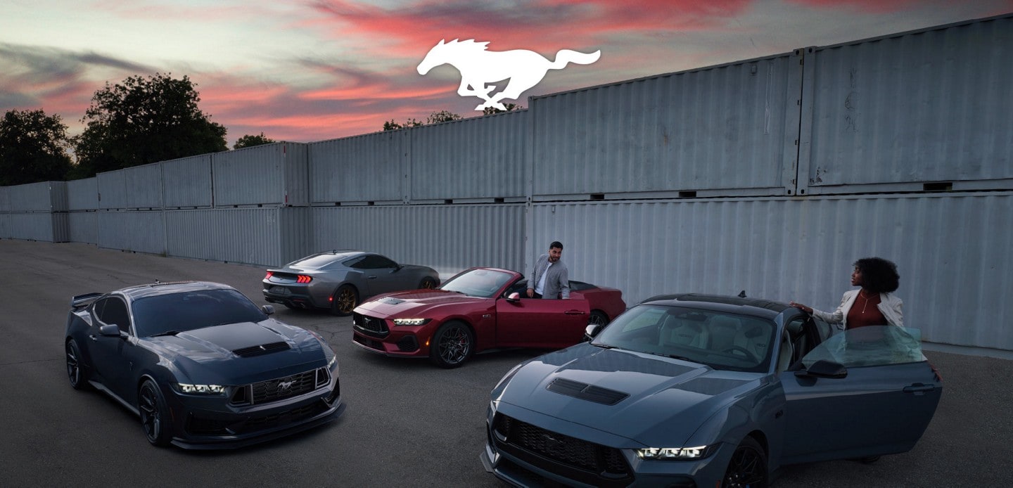 Personas subiendo en un grupo de cuatro modelos Ford Mustang® 2024 estacionados cerca de contenedores para envío