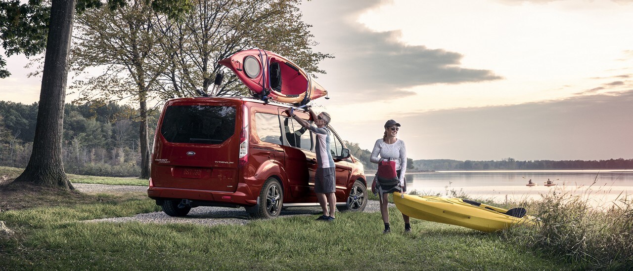 A couple unloads kayaks from the roof of a transit connect