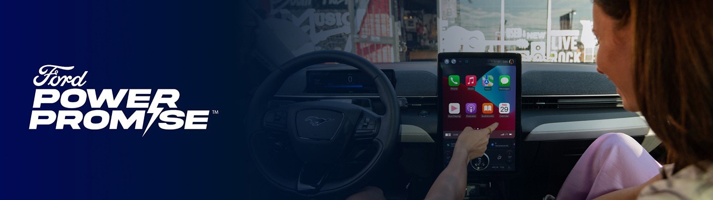 A passenger uses the touch screen of a Ford F-150 Lightning with a Ford Power Promise logo overlaid
