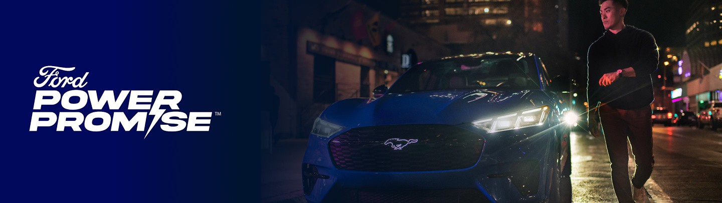 A man outside of a blue Ford Mustang Mach-E® at night with a Ford Power Promise logo overlaid