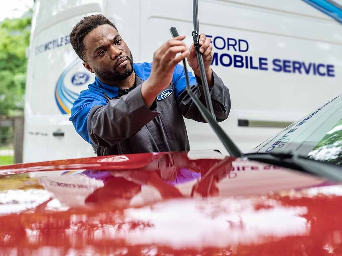 Un técnico de Servicio Ford cambia el limpiaparabrisas en un vehículo Ford. La camioneta de trabajo de Servicio Móvil está en segundo plano