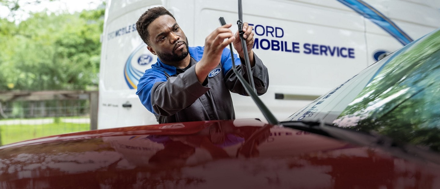 A Ford service technician changes a windshield wiper on a Ford vehicle. The Mobile Service work truck is in the background