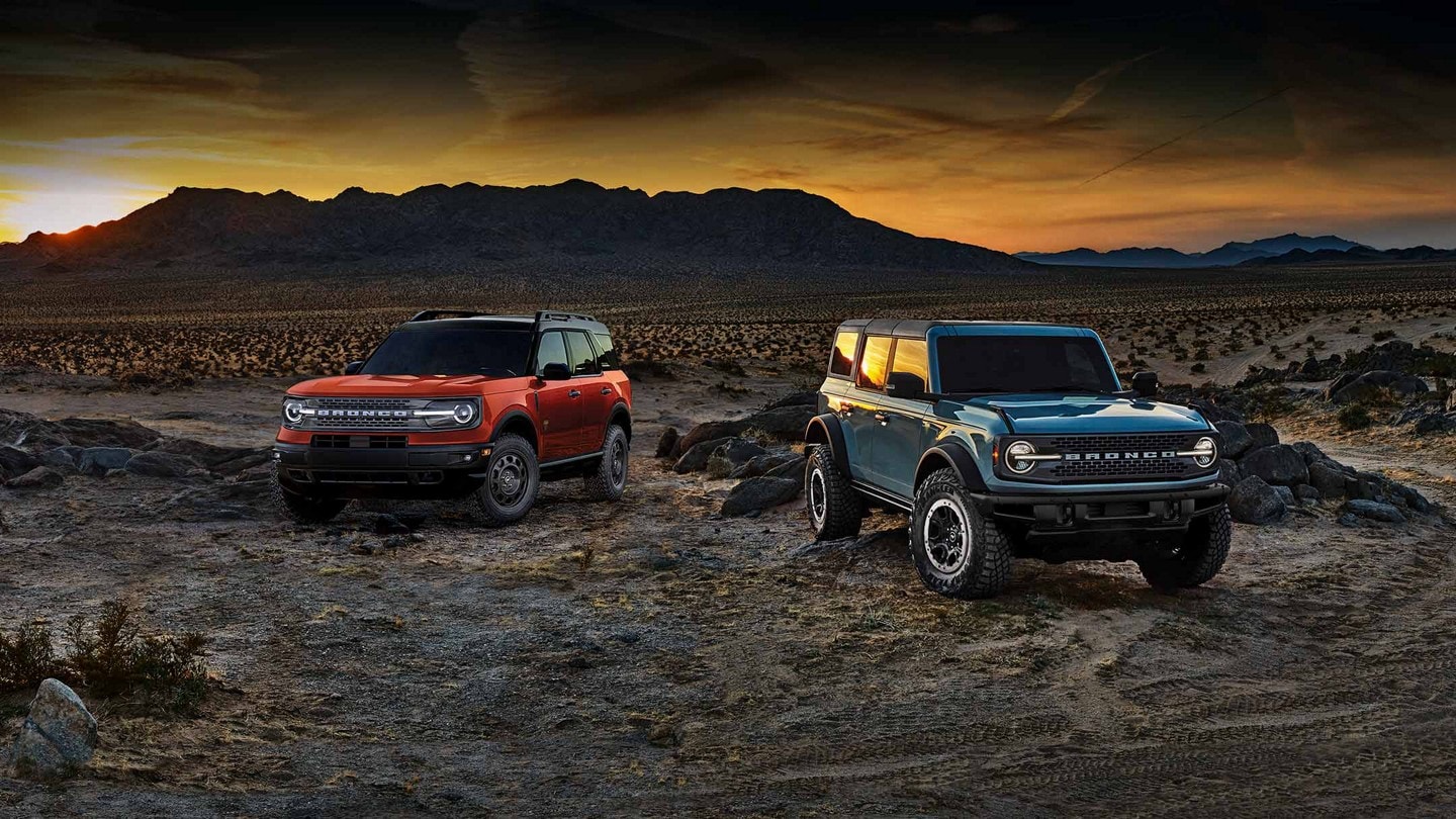 A Ford Bronco SUV and Ford Bronco Sport SUV parked among rocks and scrub in the desert