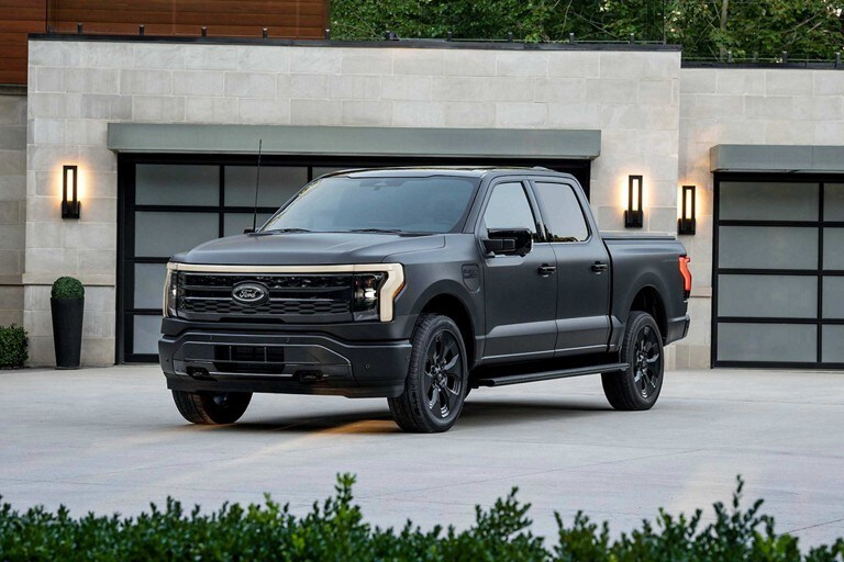  2024 Ford F-150 Lightning in matte black with black rims parked in front of modern home. 
