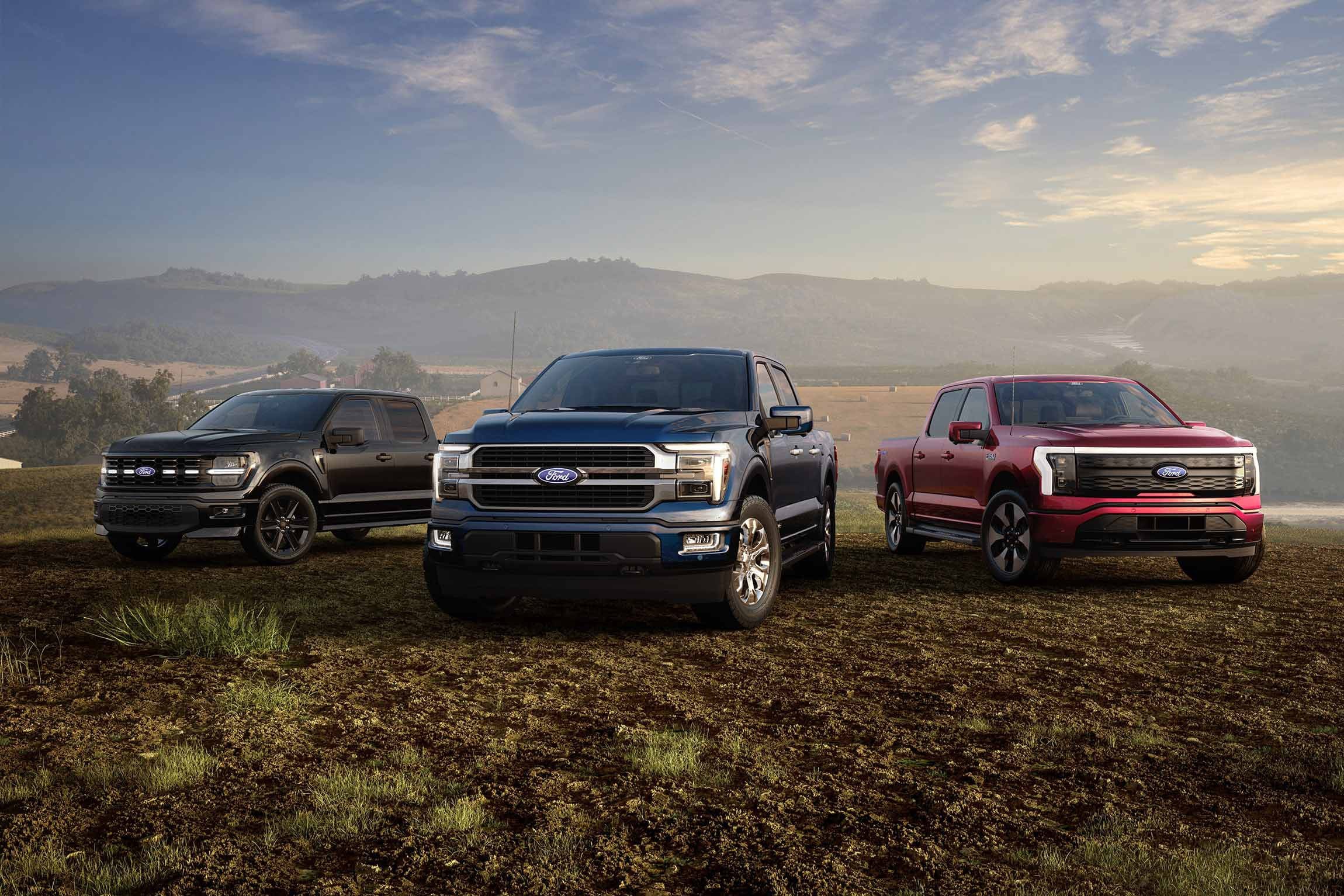 Two 2026 Ford F-150® trucks and a 2026 Ford F-150® Lightning® parked in a field in front of a mountain range