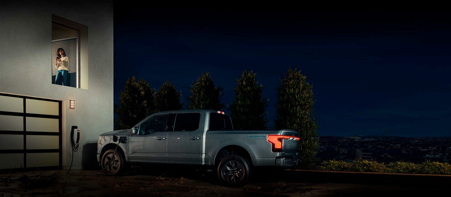 A woman checks her Ford Intelligent Backup Power smartphone app as a Ford F-150® Lightning™ is plugged into her home