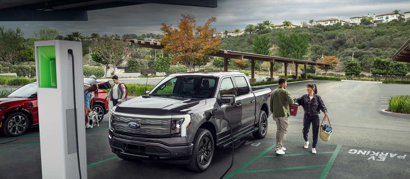 A man and woman sit on the open liftgate of a Ford F-150® Lightning™ as it charges