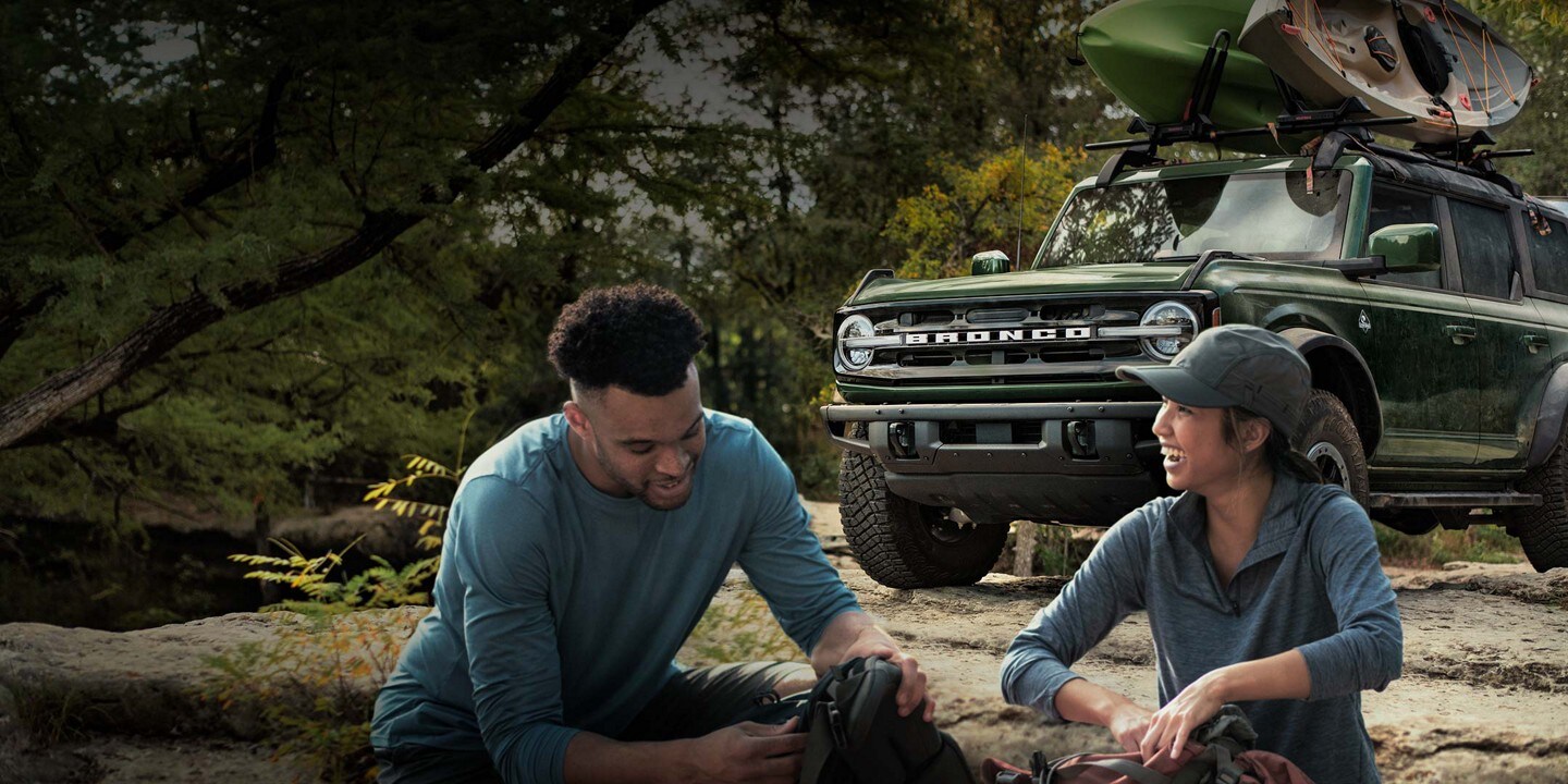 Una pareja acampando con una SUV Ford Bronco® 2023 de fondo con kayaks en el techo