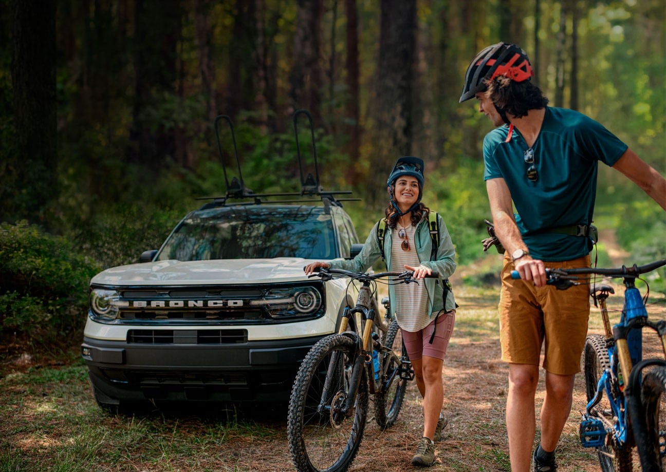 Una SUV Ford Bronco® Sport 2024 en el fondo con dos personas paradas fuera del vehículo y bicicletas