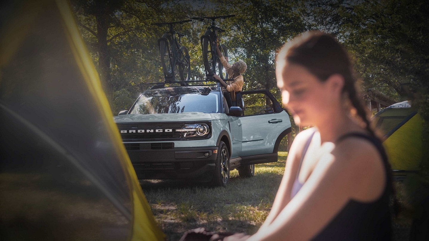 Una SUV Ford Bronco Sport® 2024 estacionada en el pasto con una mujer sujetando una bicicleta en el techo con una mujer joven parada cerca