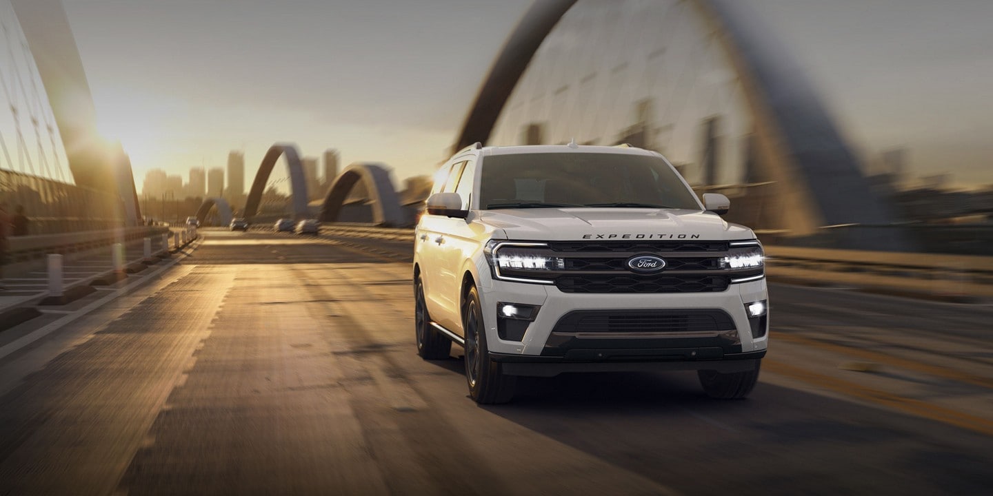 A 2024 Ford Expedition® SUV driving across a modern bridge near a city at sunset