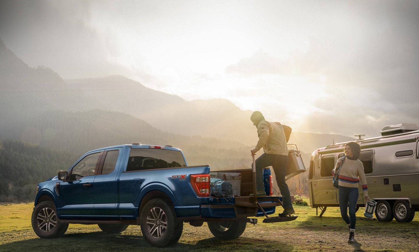 Man using the retractable tailgate step to load items into the bed of a 2023 Ford F-150® pickup