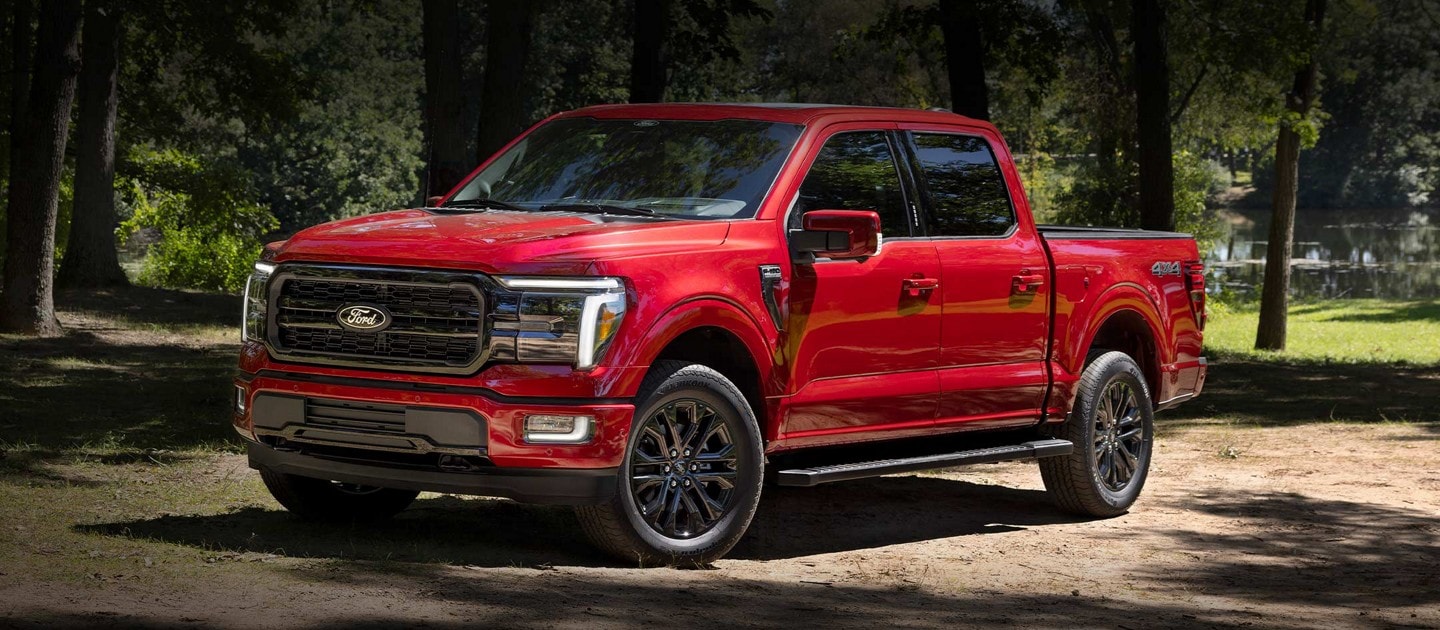 Una camioneta Ford F-150® LARIAT® 2024 en Rapid Red con el Paquete de Apariencia Black estacionada en un entorno rústico