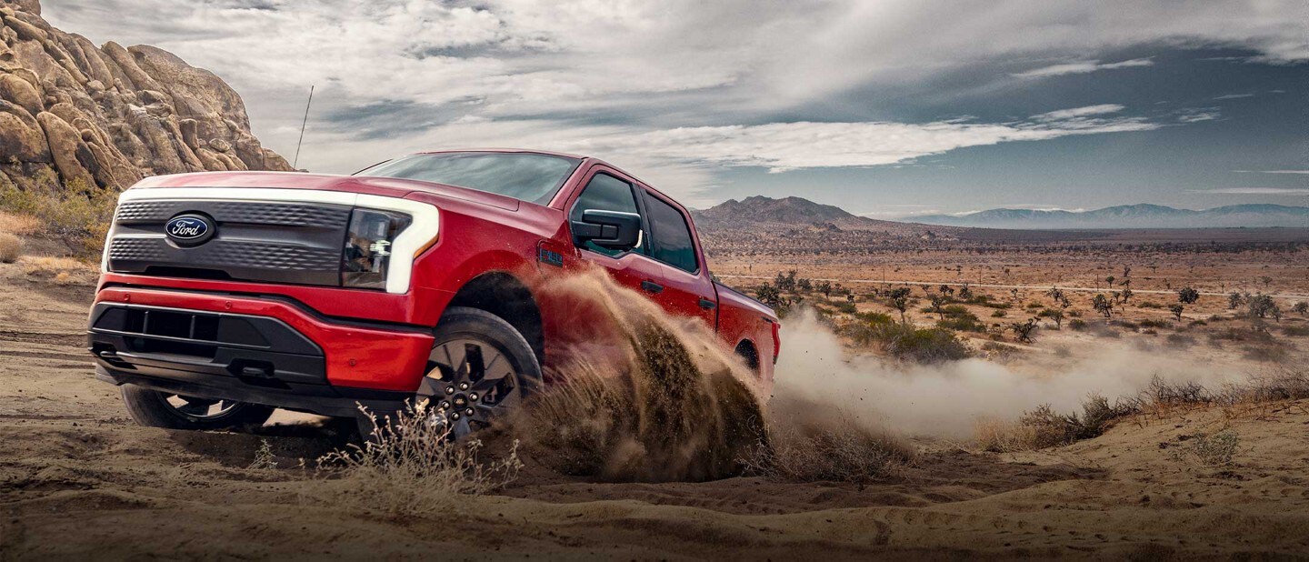 A red 2024 Ford F-150 Lightning® pickup truck drives at speed across a sandy landscape