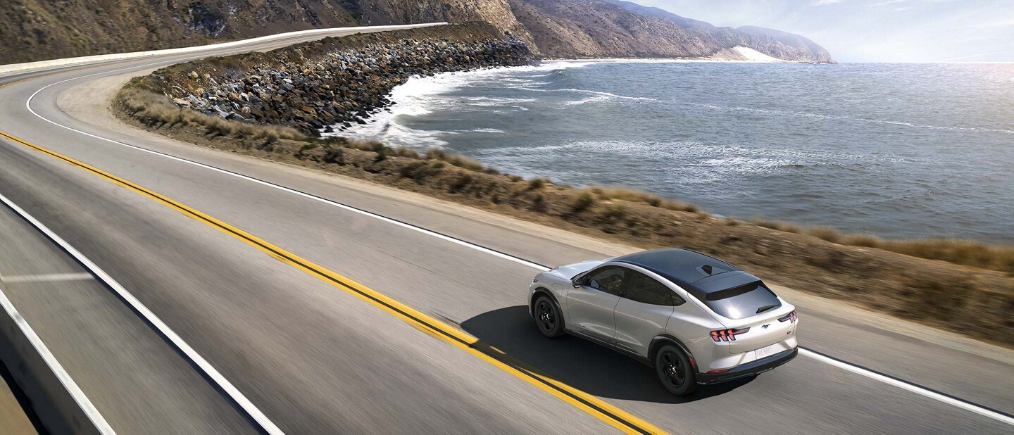 A Silver 2023 Ford Mustang Mach-E driving down the road along the ocean