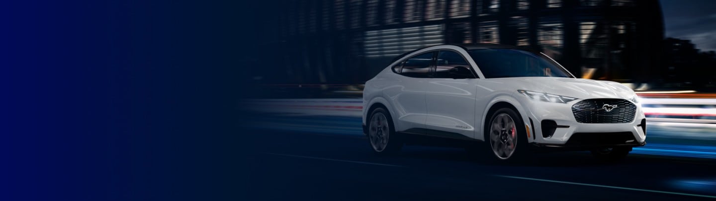 2024 Ford Mustang Mach-E® being driven down a city street with a Ford Power Promise logo overlaid