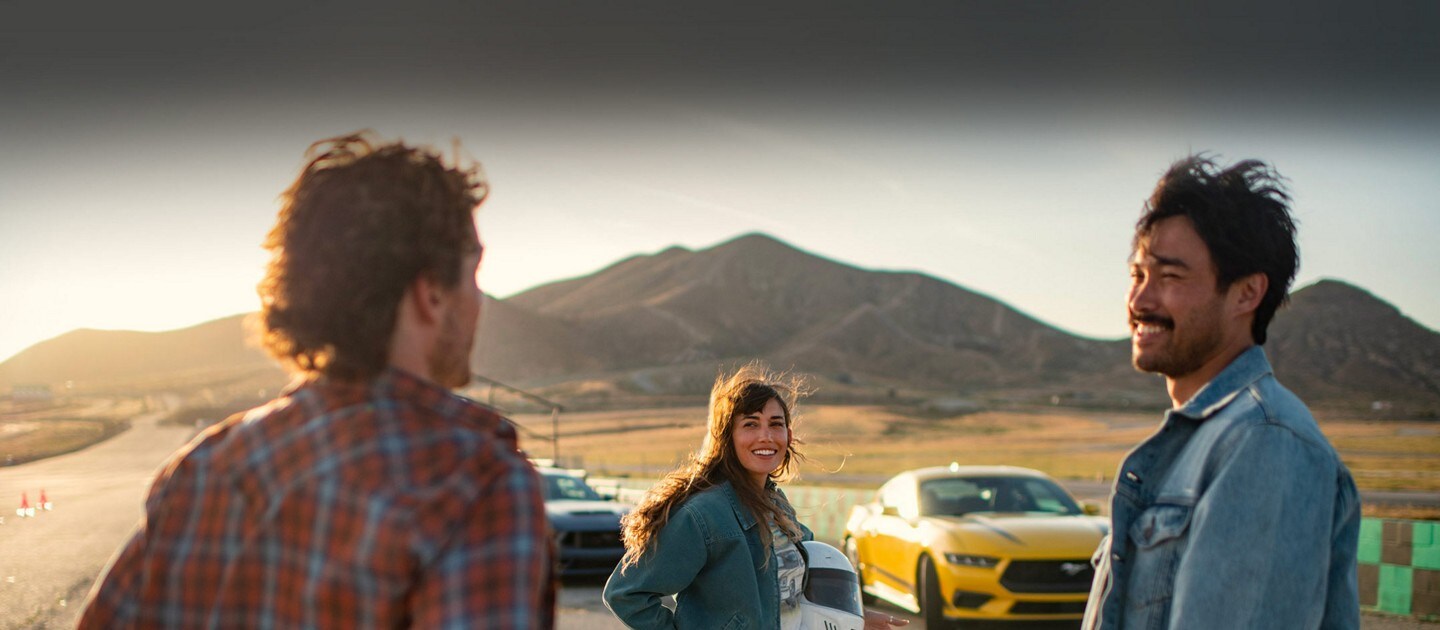 Dos modelos Ford Mustang® 2024 estacionados cerca de un hipódromo con tres personas cerca